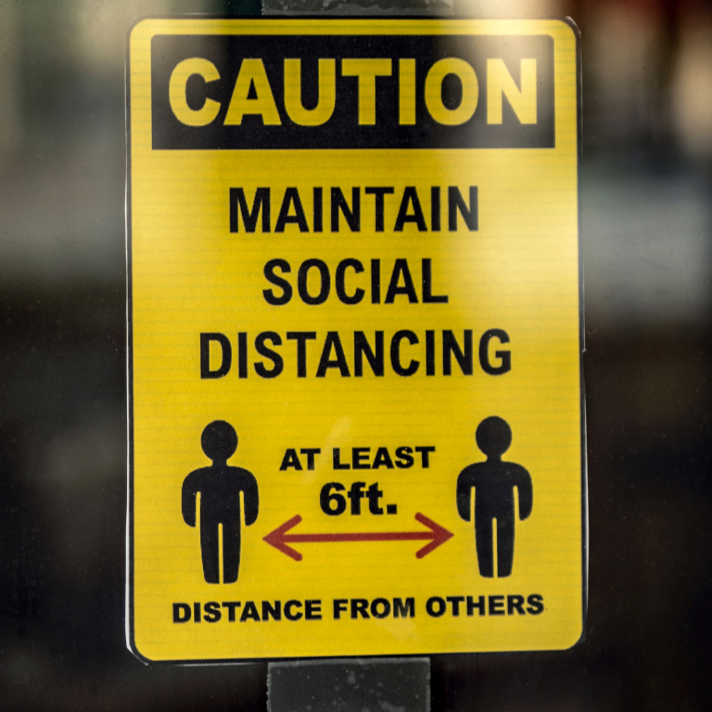 A sign that says Caution Maintain Social Distancing. At least 6 ft. Distance from others. With two stick drawings and an arrow. 