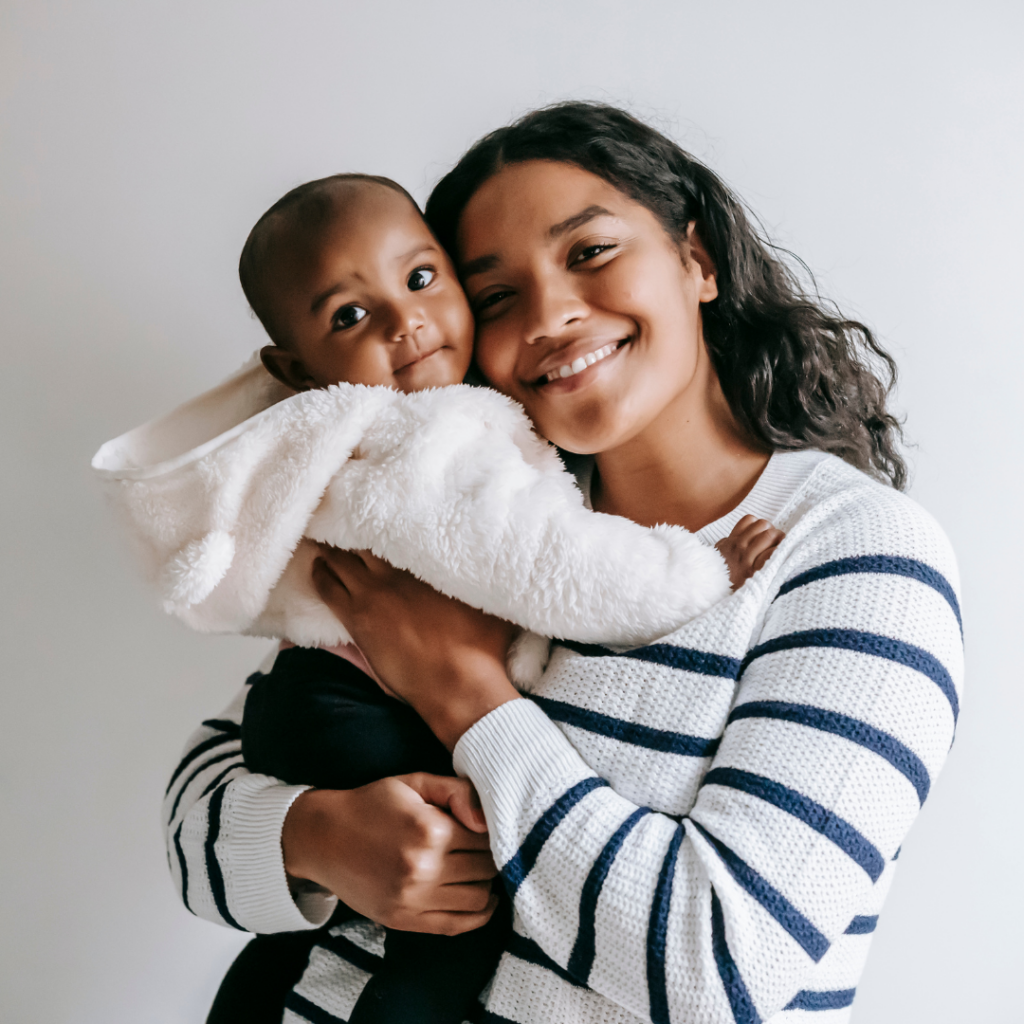 A young black mother holding a small toddler. The toddler is wearing a white coat. Arundel House of Hope helps mothers in recovery